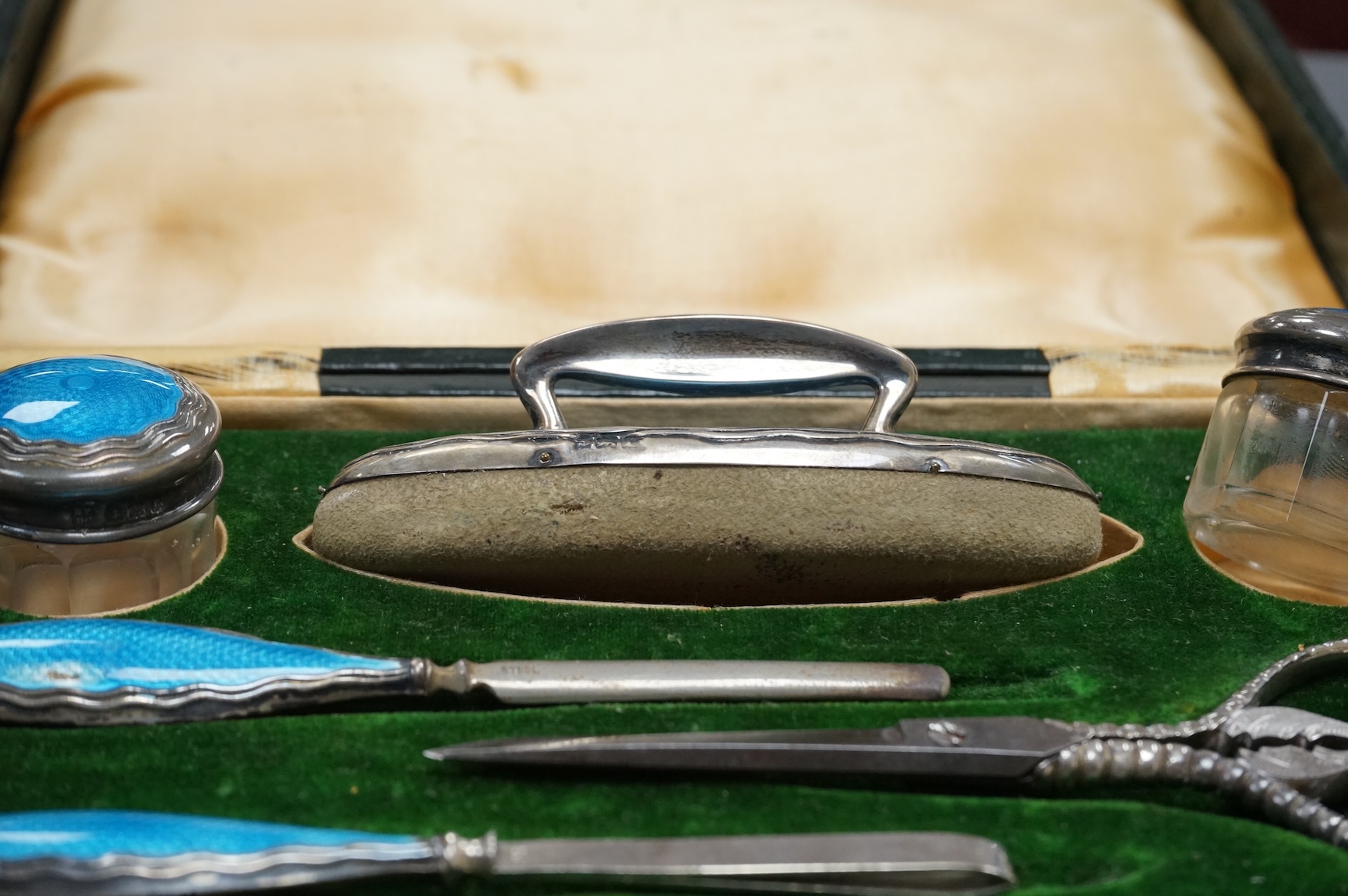 A cased George V eight piece (ex 9 piece) manicure and toilet jar set, comprising seven silver and enamel mounted items, Boots Pure Drug Company, Chester and Birmingham, 1910, together with a matching pair of steel sciss